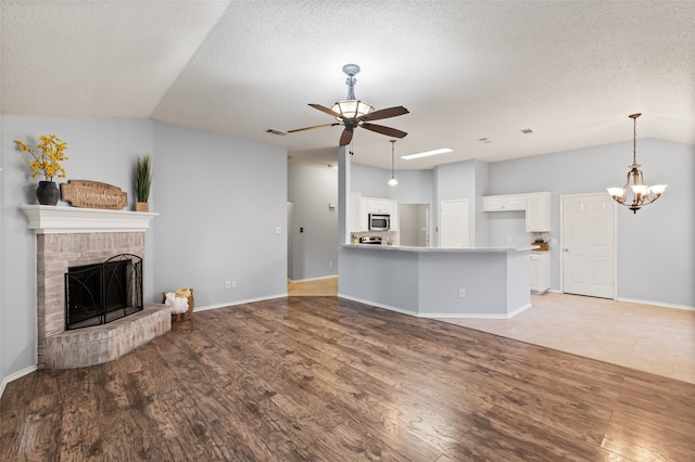 unfurnished living room featuring a fireplace, light wood-type flooring, vaulted ceiling, a textured ceiling, and ceiling fan with notable chandelier