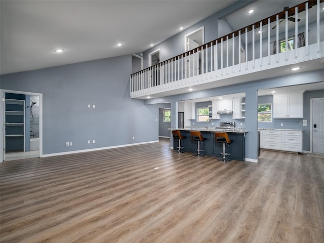 unfurnished living room with light wood-style flooring, a sink, baseboards, recessed lighting, and high vaulted ceiling