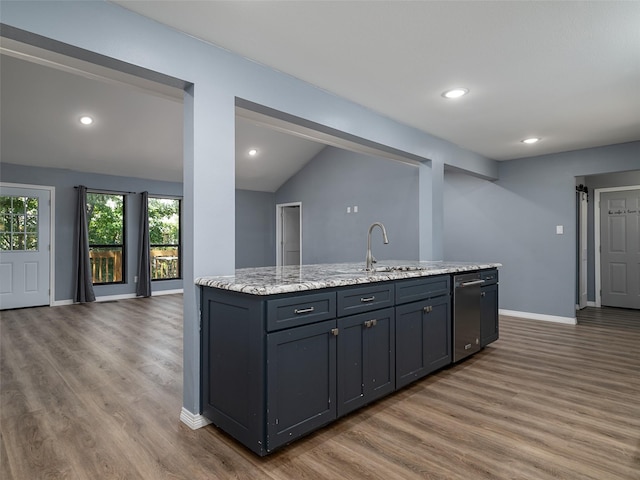 kitchen featuring vaulted ceiling, wood finished floors, stainless steel dishwasher, and a sink