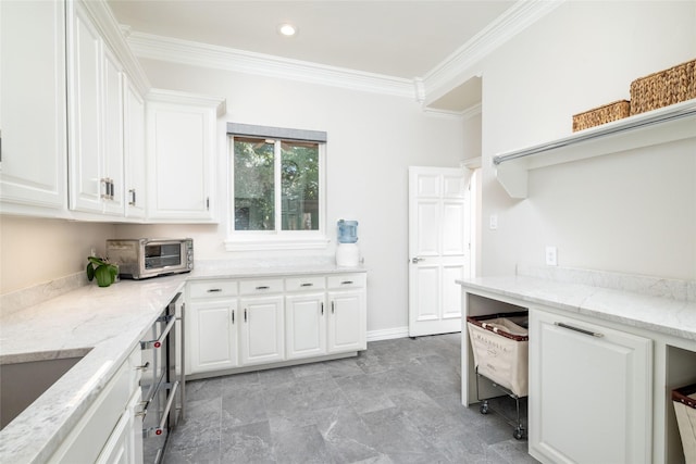 kitchen featuring light stone countertops, a toaster, white cabinets, a sink, and crown molding