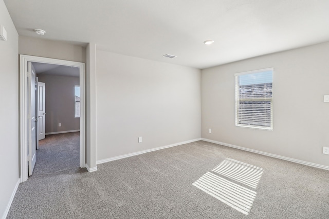 empty room with baseboards, visible vents, and carpet floors