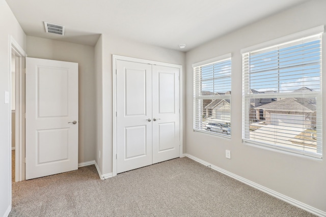 unfurnished bedroom featuring a closet, visible vents, light colored carpet, and baseboards
