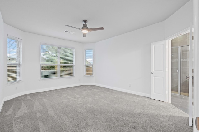 carpeted spare room with a ceiling fan, visible vents, baseboards, and plenty of natural light