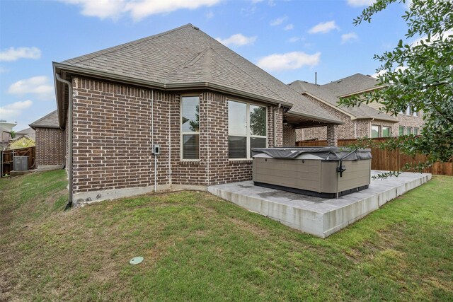 rear view of house featuring roof with shingles, a fenced backyard, brick siding, and a hot tub