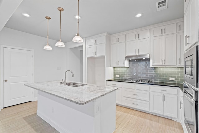kitchen with stainless steel appliances, under cabinet range hood, backsplash, a sink, and white cabinetry