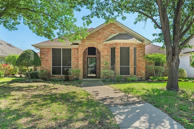 view of front facade featuring a shingled roof, brick siding, and a front lawn