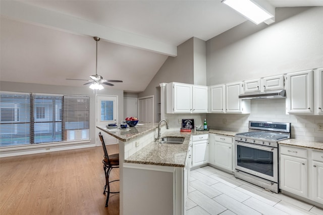 kitchen with a sink, under cabinet range hood, gas stove, a peninsula, and backsplash