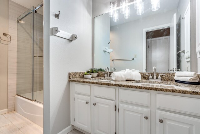full bath with shower / bath combination with glass door, double vanity, a sink, and baseboards