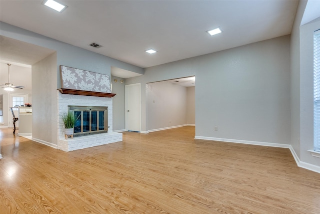 unfurnished living room featuring a brick fireplace, ceiling fan, light wood-type flooring, visible vents, and baseboards