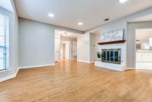 unfurnished living room with baseboards, visible vents, light wood-style floors, and a fireplace