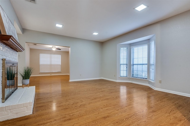 unfurnished living room with wood finished floors, ceiling fan, baseboards, and a brick fireplace
