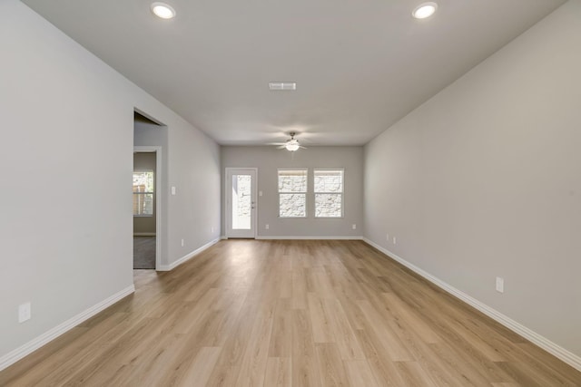 empty room featuring light wood-style floors, a healthy amount of sunlight, a ceiling fan, and baseboards