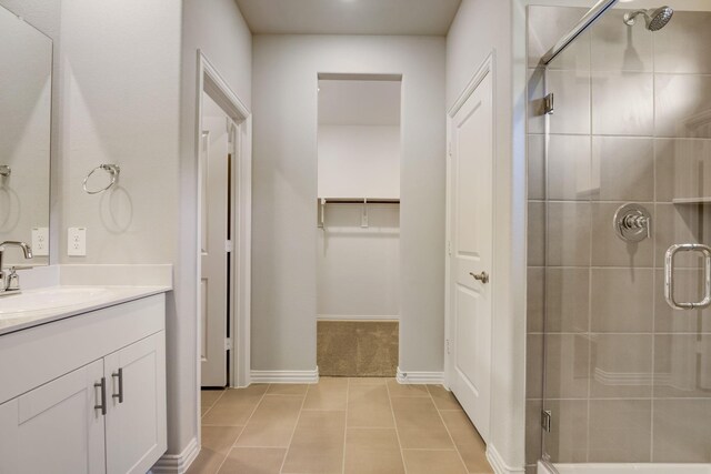 full bath featuring baseboards, tile patterned flooring, a shower stall, vanity, and a walk in closet
