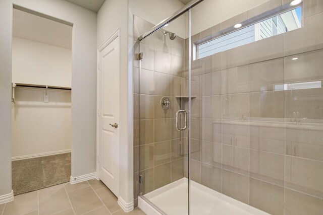 full bathroom with tile patterned flooring, a walk in closet, a shower stall, and baseboards