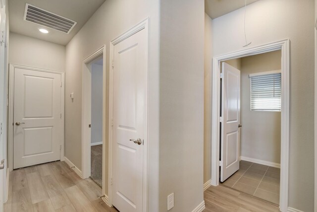 hall with baseboards, visible vents, and light wood-style floors