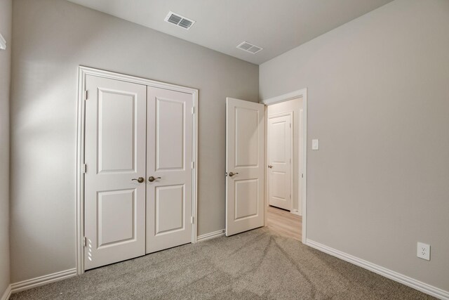unfurnished bedroom with baseboards, visible vents, light carpet, and a closet
