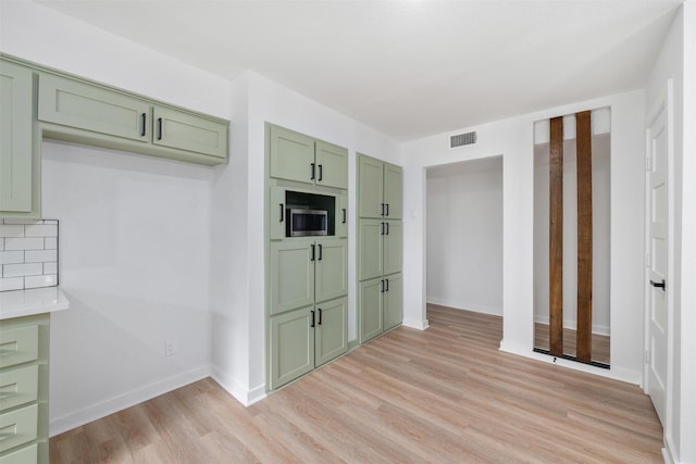 kitchen with stainless steel microwave, light wood-style floors, green cabinets, visible vents, and baseboards