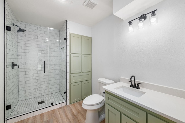 bathroom with a shower stall, visible vents, toilet, wood finished floors, and vanity
