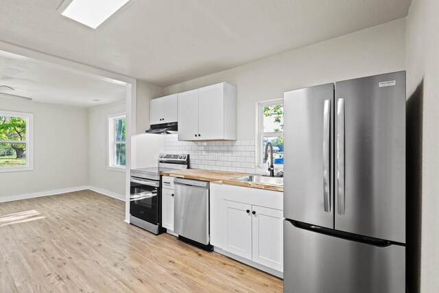 kitchen featuring a sink, stainless steel appliances, tasteful backsplash, light wood-type flooring, and white cabinets