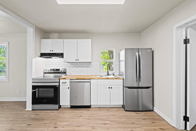 kitchen with wood counters, a sink, appliances with stainless steel finishes, under cabinet range hood, and backsplash