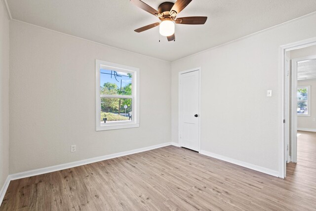 empty room featuring light wood-type flooring, crown molding, a ceiling fan, and baseboards