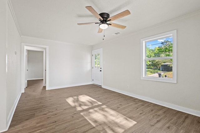 empty room featuring wood finished floors, ornamental molding, ceiling fan, baseboards, and visible vents