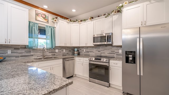 kitchen featuring light stone countertops, a sink, decorative backsplash, white cabinetry, and appliances with stainless steel finishes
