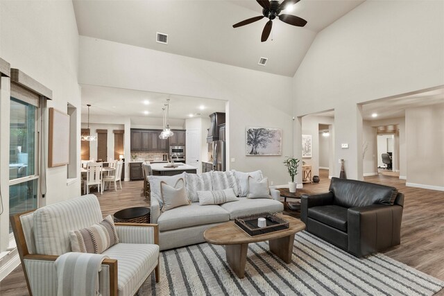 living room with visible vents, high vaulted ceiling, wood finished floors, and ceiling fan with notable chandelier