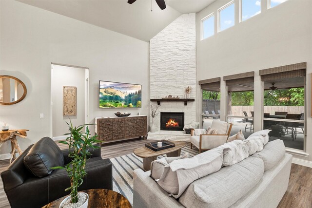 living room featuring baseboards, a fireplace, wood finished floors, a ceiling fan, and high vaulted ceiling