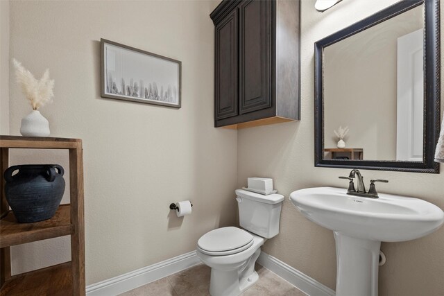 half bathroom featuring baseboards, toilet, tile patterned flooring, and a sink