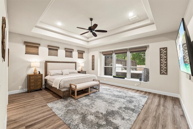 bedroom with wood finished floors, ceiling fan, baseboards, visible vents, and a raised ceiling