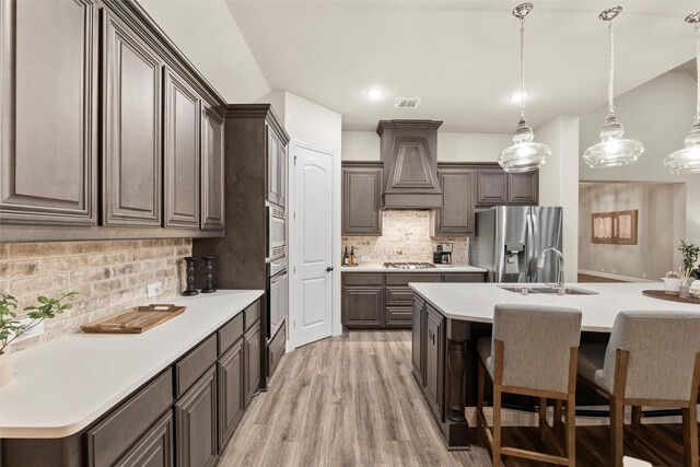 kitchen with custom range hood, dark brown cabinets, stainless steel appliances, and tasteful backsplash