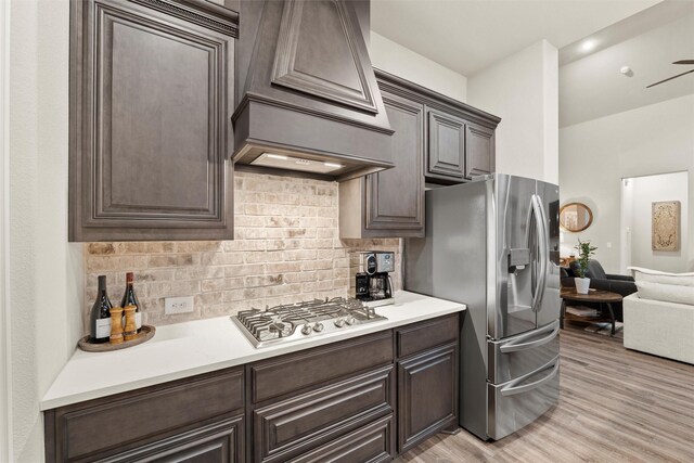 kitchen with dark brown cabinetry, custom range hood, appliances with stainless steel finishes, and light countertops