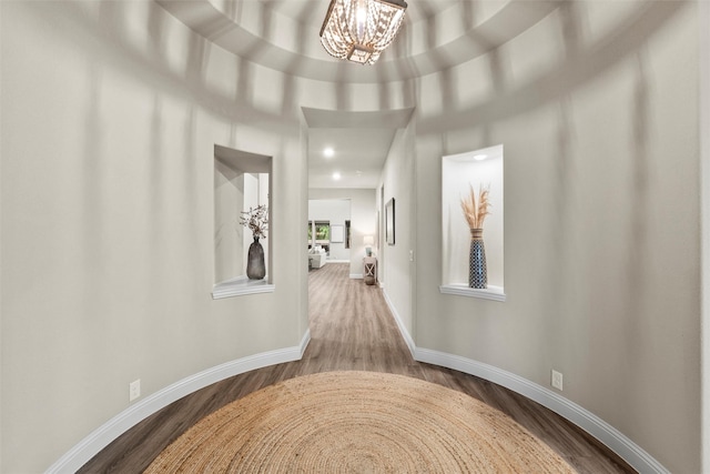 hallway with wood finished floors, recessed lighting, a chandelier, and baseboards