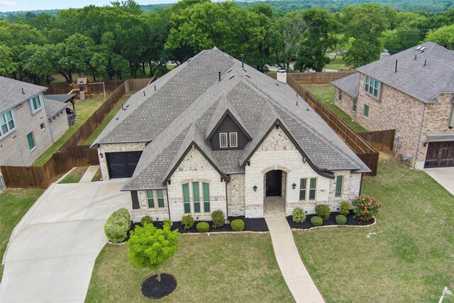 french country style house featuring a fenced backyard, roof with shingles, concrete driveway, and stone siding