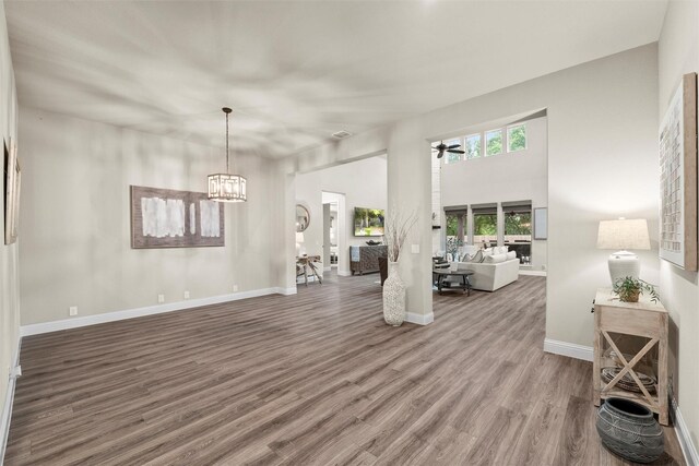living room featuring wood finished floors, ceiling fan with notable chandelier, and baseboards
