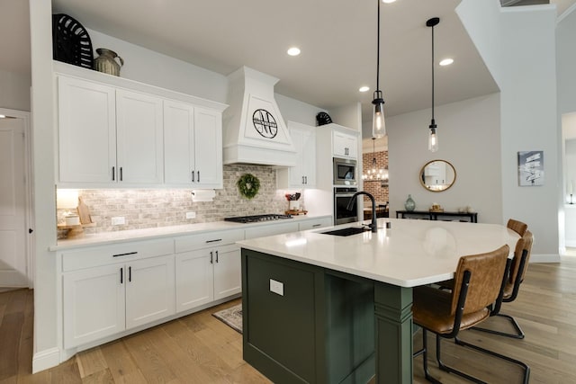 kitchen with decorative backsplash, appliances with stainless steel finishes, a sink, premium range hood, and light wood-style flooring