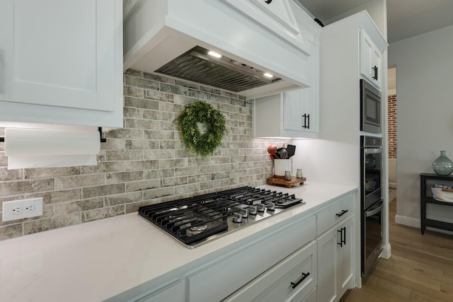kitchen with light countertops, stainless steel appliances, white cabinetry, wood finished floors, and custom exhaust hood