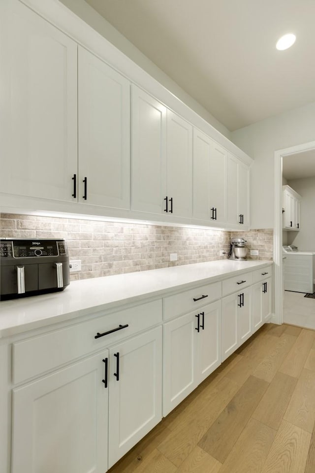 kitchen with white cabinets, light countertops, tasteful backsplash, and light wood-style floors