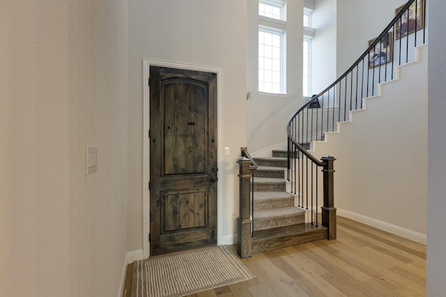 foyer entrance with light wood-style floors, baseboards, a high ceiling, and stairway