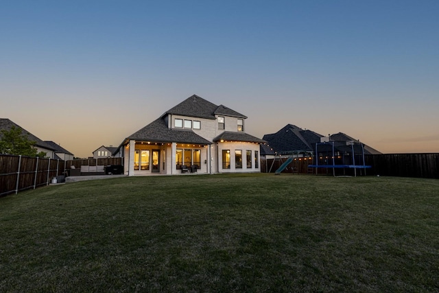 back of property at dusk with a lawn, a fenced backyard, a trampoline, and a patio area