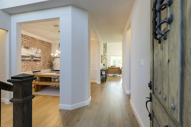 corridor featuring brick wall, a notable chandelier, baseboards, and light wood-style floors