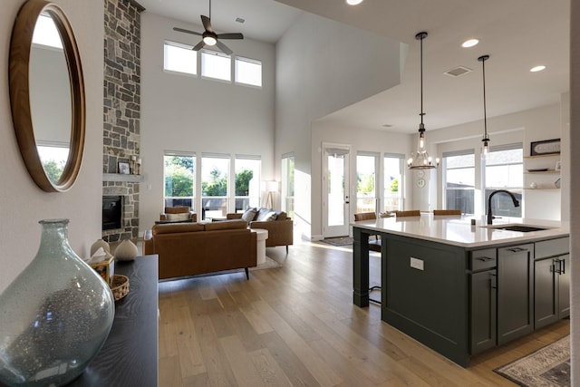 kitchen featuring a sink, ceiling fan with notable chandelier, light wood finished floors, and a stone fireplace