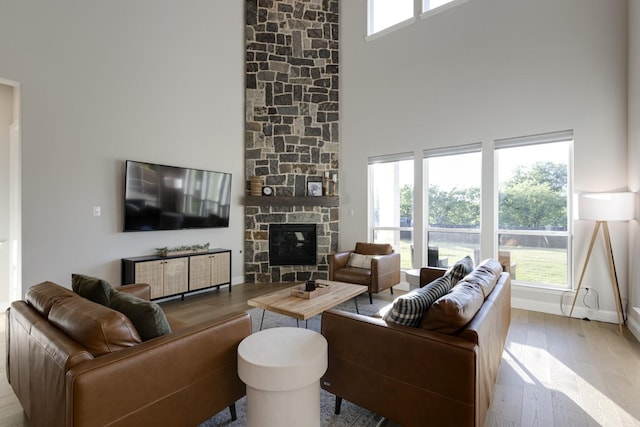 living room featuring baseboards, a stone fireplace, wood finished floors, and a towering ceiling