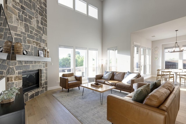 living room with baseboards, hardwood / wood-style flooring, a stone fireplace, and a towering ceiling