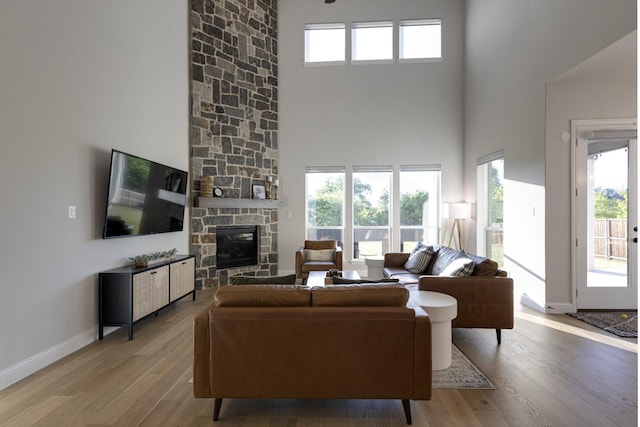 living area featuring baseboards, a high ceiling, a stone fireplace, and wood finished floors