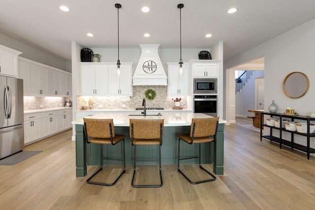kitchen with decorative backsplash, a center island with sink, light countertops, custom range hood, and stainless steel appliances