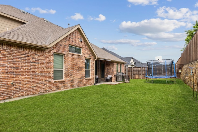 back of house with a trampoline, brick siding, a shingled roof, and a patio