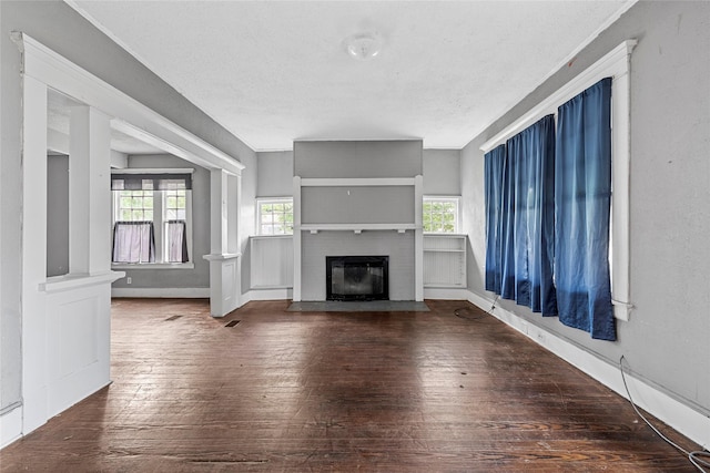 unfurnished living room with hardwood / wood-style floors, a wealth of natural light, a textured ceiling, and a fireplace with flush hearth