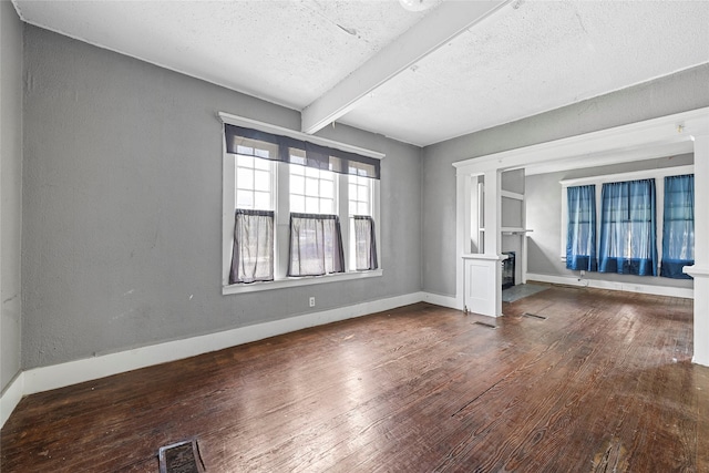 unfurnished room featuring beamed ceiling, visible vents, baseboards, a textured ceiling, and hardwood / wood-style floors